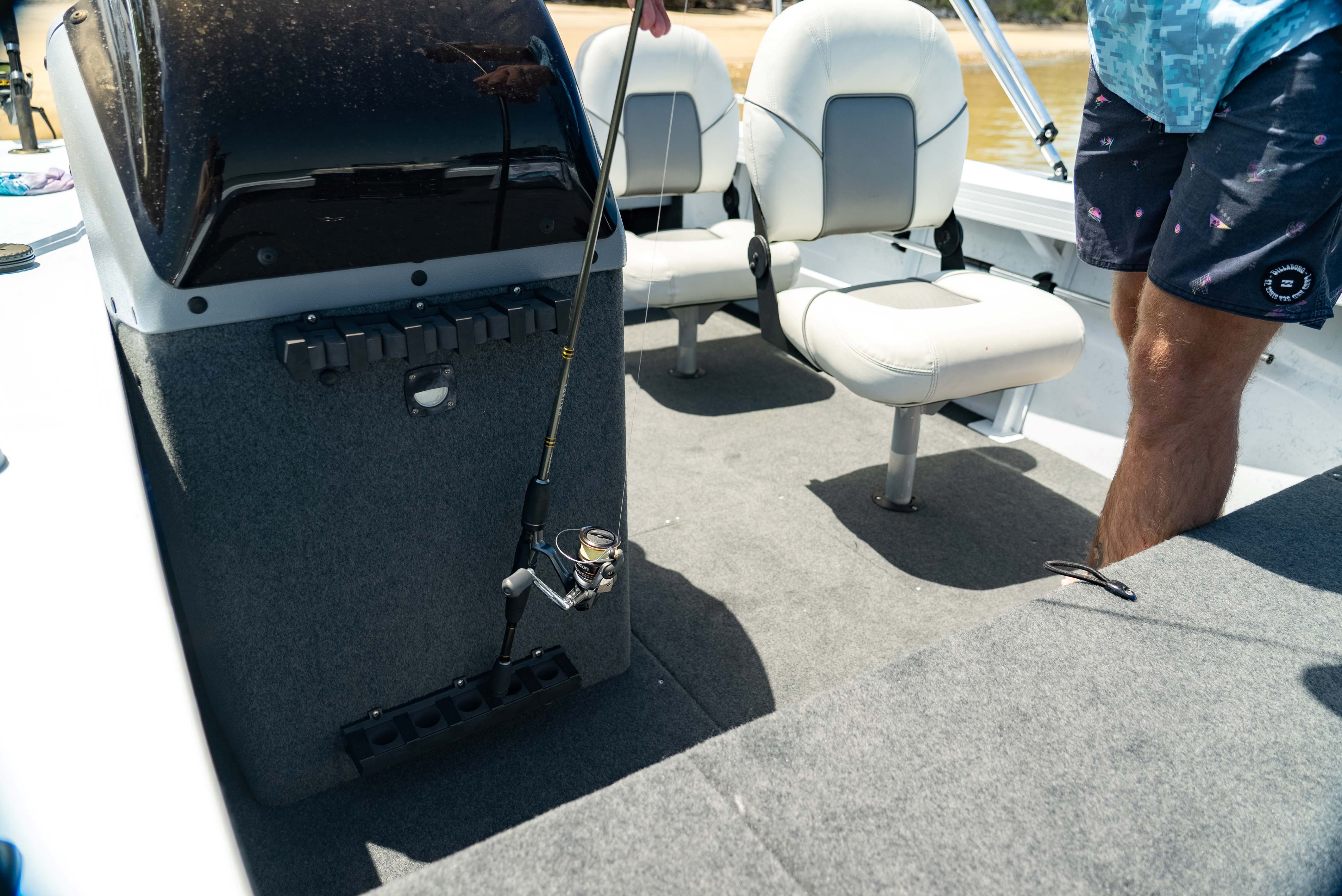 Interior of a Quintrex boat featuring white swivel seats and a fishing rod mounted to a grey carpeted console.